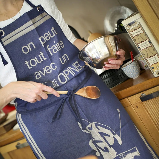 An adult wearing a blue apron with 'Opinel' branding and a graphic of a person skiing, standing in a kitchen environment.