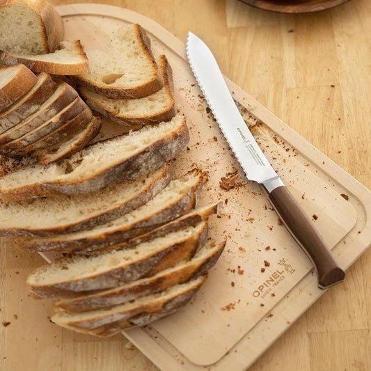 A slicing bread on a beige wooden cutting board with a serrated knife placed alongside, all presented on a wooden surface.